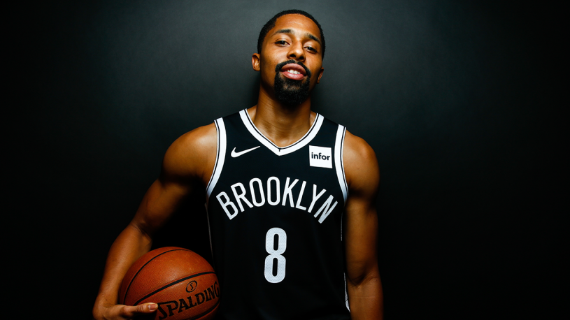 Athlete Spencer Dinwiddie wearing a Brooklyn Nets jersey and posing with a basketball after tokenizing his NBA contract