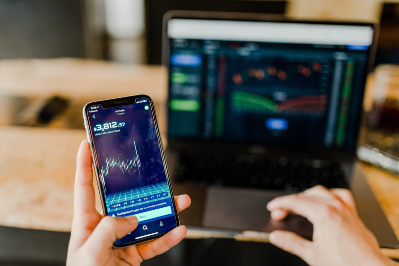 Person holding smartphone and using laptop to pay Bitcoin taxes.