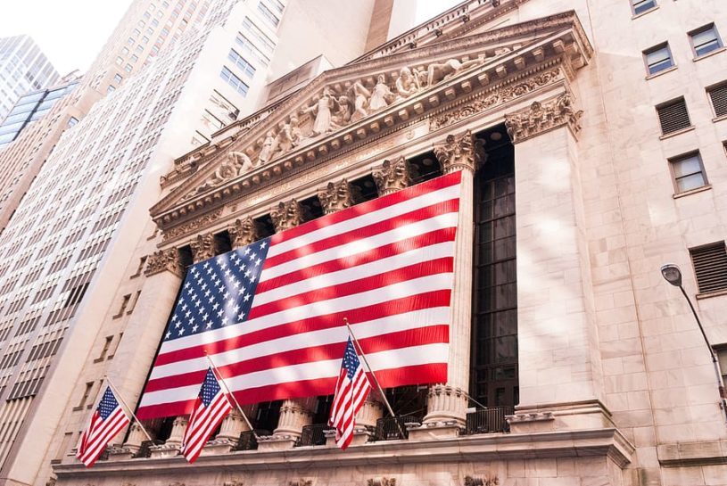 Outside picture of the New York Stock Exchange from Wall Street, with American flags everywhere.