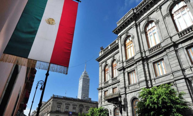 Mexican flag hanging with blue sky and financial building in background