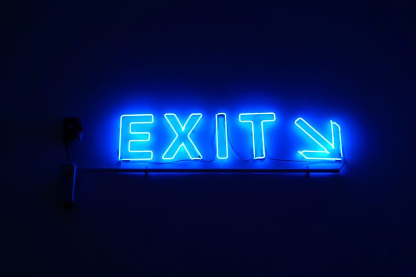 Exit sign in blue neon lights with dark blue background and arrow pointing to the bottom right