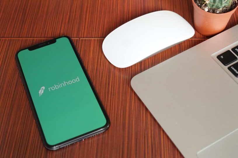 Robinhood app opened on an iPhone next to a grey apple computer and a mouse.