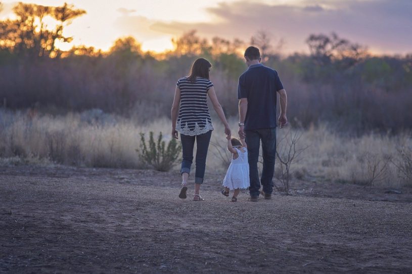 Father and mother holding child on an outdoor walk and planning for the future financially with Acorns early