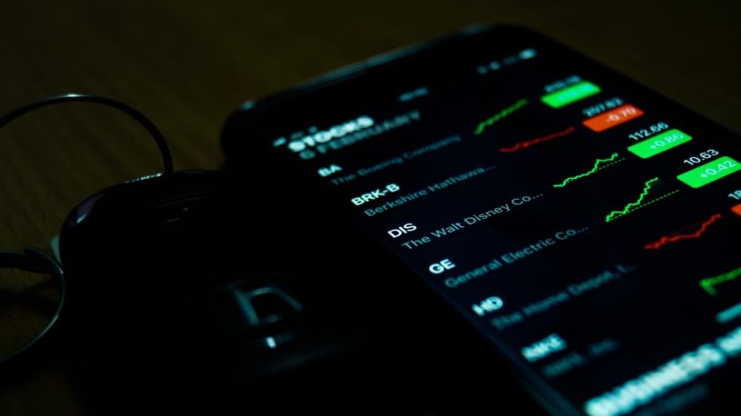 iPhone sitting on a table, turned on, with an illuminated screen displaying cheap tech stocks