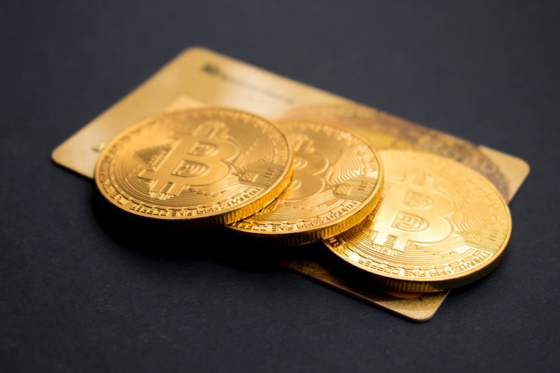 Three tokens, symbolizing bitcoin, resting on a debit card to illustrate bitcoin used in DeFi