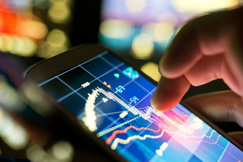 Investor using smartphone to trade the top value stocks at night with blurry lights in the background.