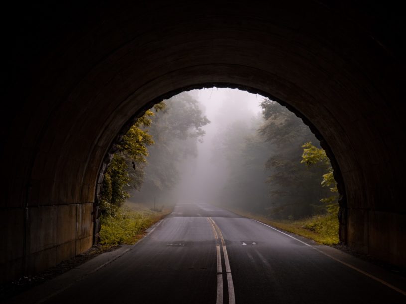 Paved road leading through a tunnel signifying the light at the end of the tunnel.