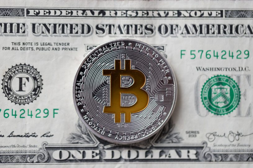 Metal Bitcoin coin on top of a $1 USD note.