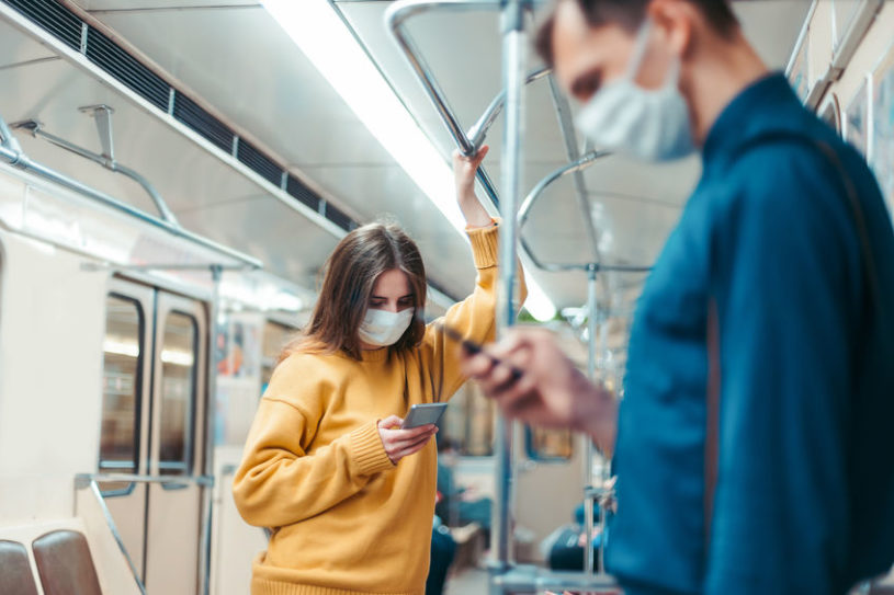 A male and female millennial on a train wearing masks and searching on their phone for the top stocks to buy in q4 2020.