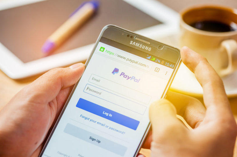 Man holding a cell phone and using it to buy Bitcoin through PayPal