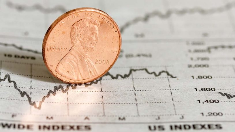 US Penny sitting on a newspaper showing financial charts of the top penny stocks to buy