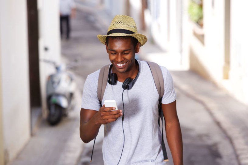 African-American millennial male checking out the top stocks on Robinhood on his iPhone while wearing a beige hat.