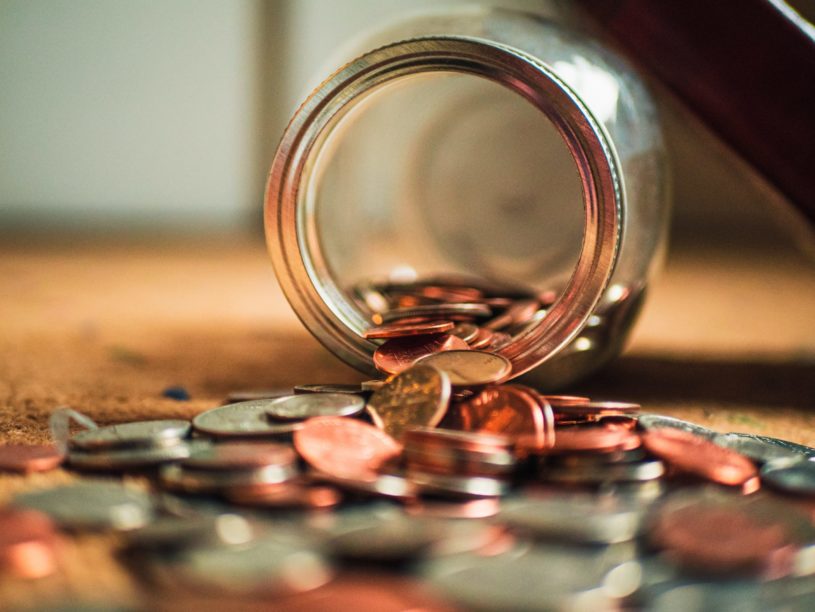 Jar on a wooden table spilling pennies and coins.