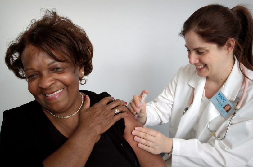 White woman administering a COVID-19 vaccine to an older black woman on the arm as they both smile