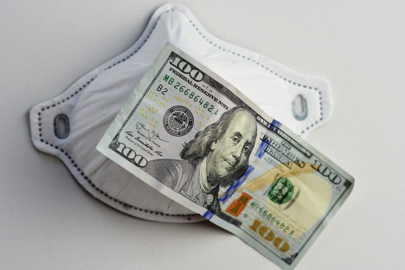 $100 USD note laying on top of a face mask used during COVID-19.