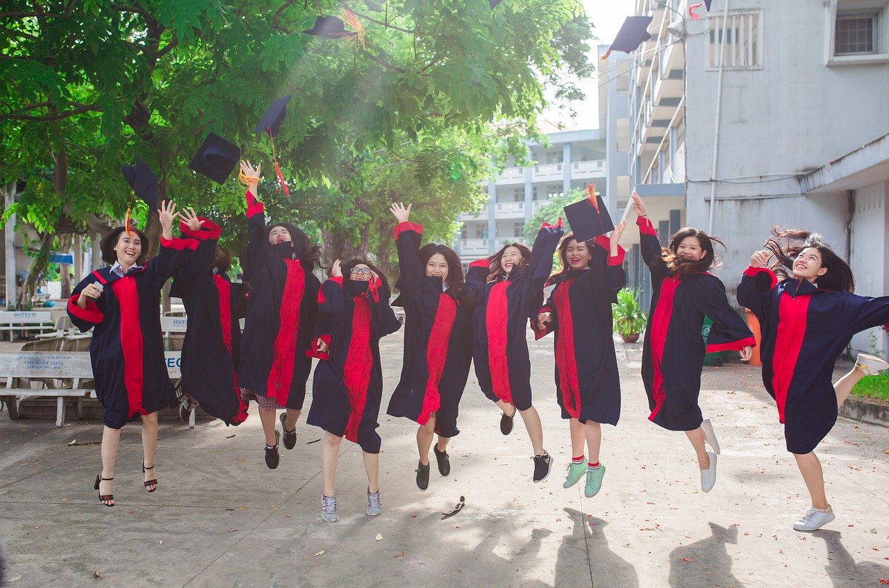 Students celebrating their graduation by jumping in the air and throwing their graduation caps.