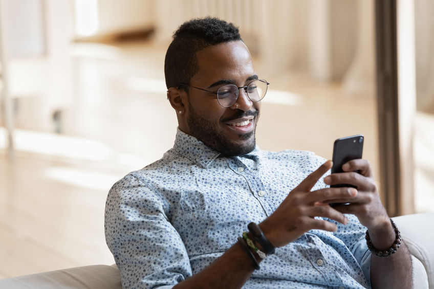 Smiling young african American man in glasses looking at his phone to find the top stocks under $1 on Robinhood's stock trading app.