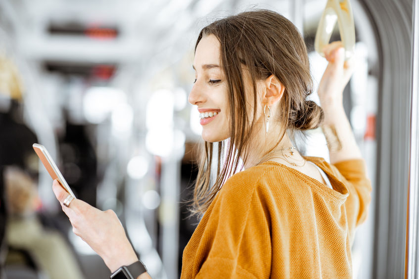 Close-up portrait of a young woman using smartphone while standing in the modern tram and researching the top tech stocks in early 2021.