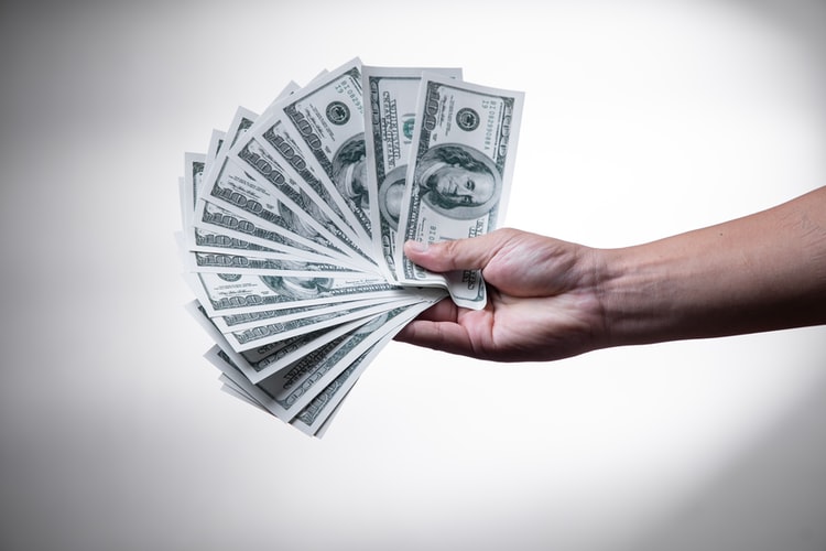 Outstretched hand ostentatiously spreading dollar bills.