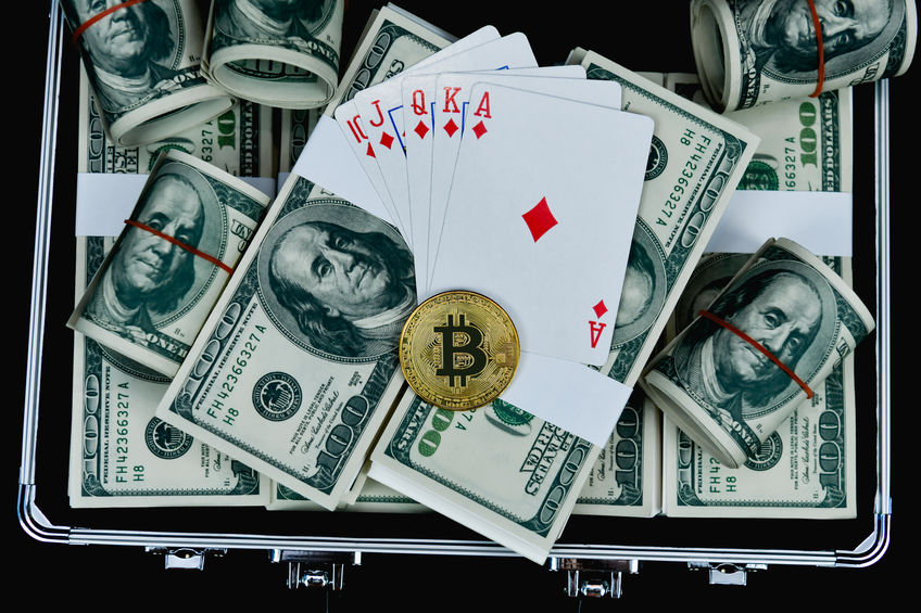 Several $100 USD notes in a brief case, with a royal flush of playing cards and a single, gold, bitcoin.