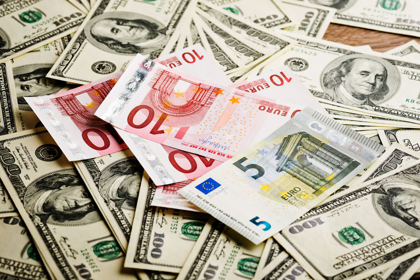 Several $100 USD notes on a table with a few 10 and 5 Euro notes on top