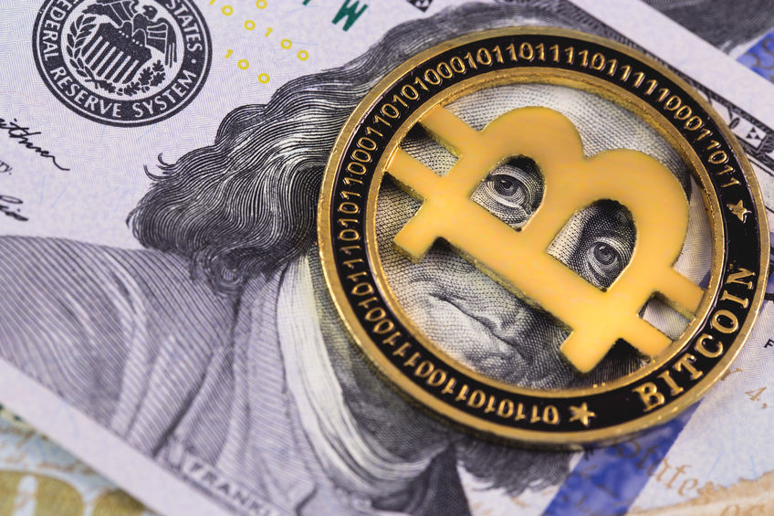 $100 USD note with a gold bitcoin token on top of Benjamin Franklin's face.