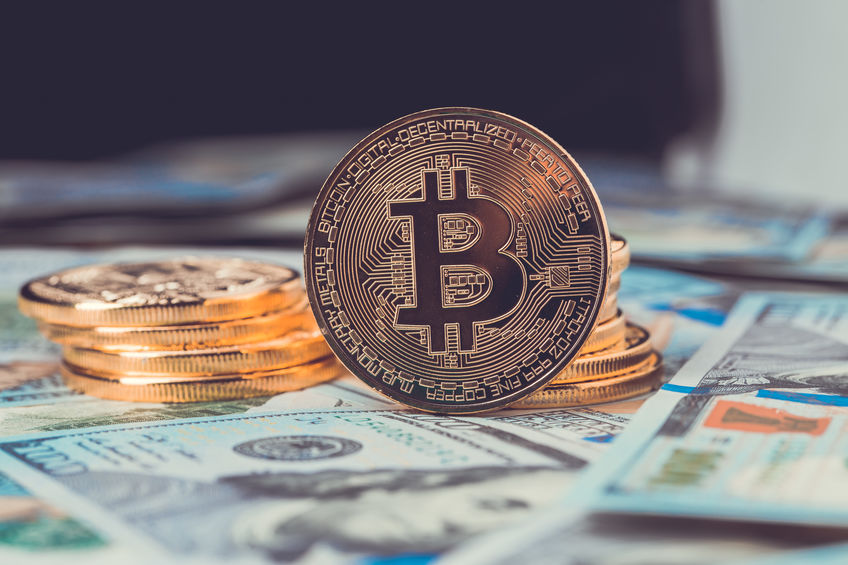 Bitcoin tokens sitting on several $100 USD notes.