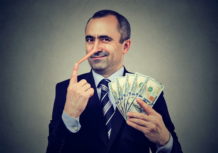 Business man wearing suit holding $100 USD notes with a growing nose to signifying lying and fraud.