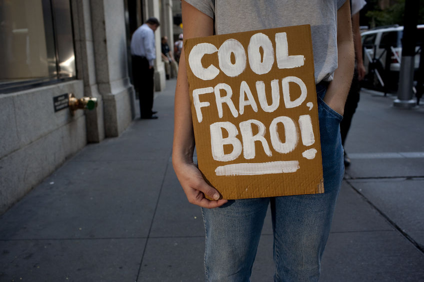 Millennial male standing on Wall Street with a sign that says "Cool fraud, bro!"