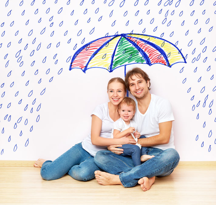 Young married couple sitting down on wooden floor, holding a newborn baby and an umbrella which keeps them dry from rain.