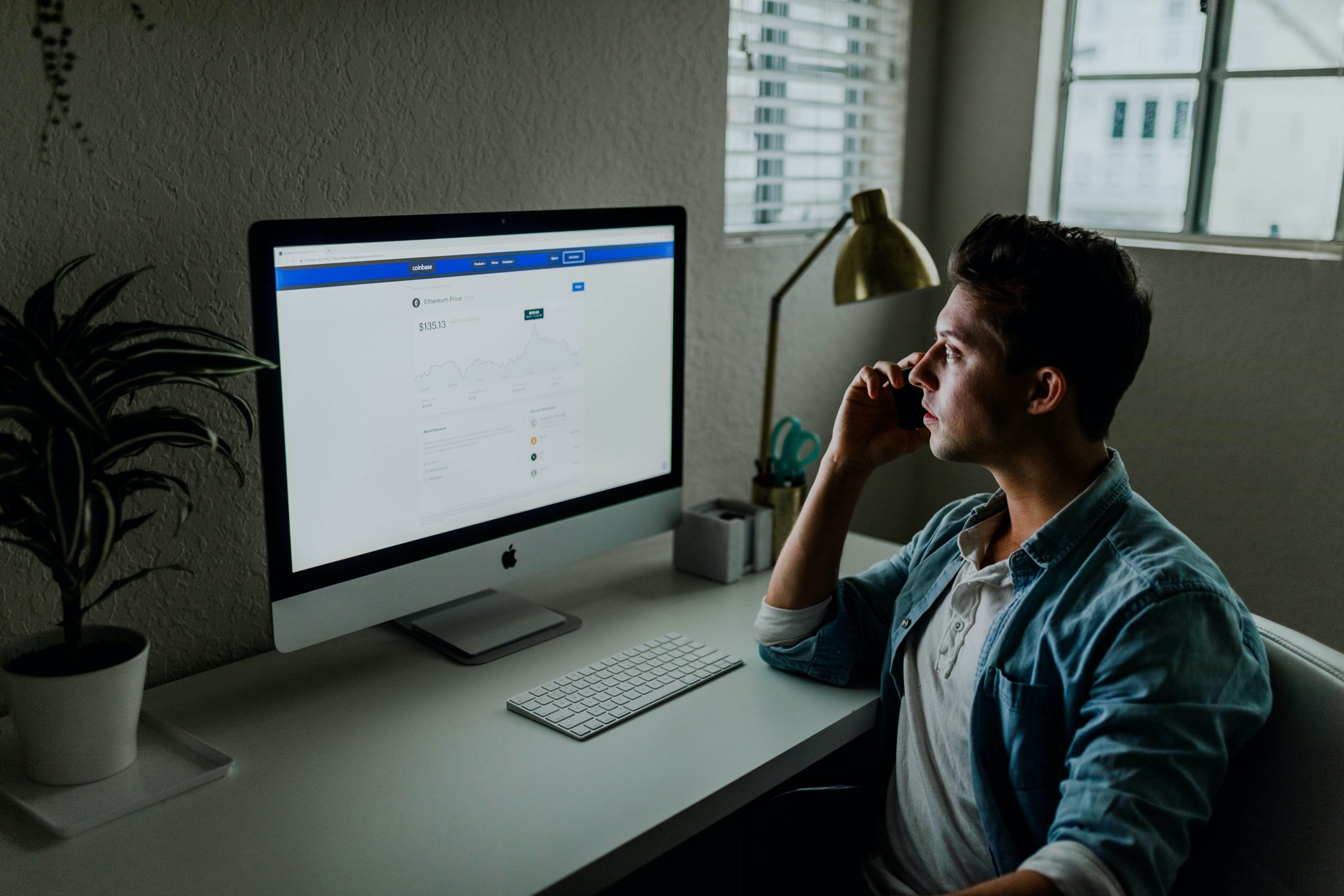 A man in blue shirt, facing a Mac monitor