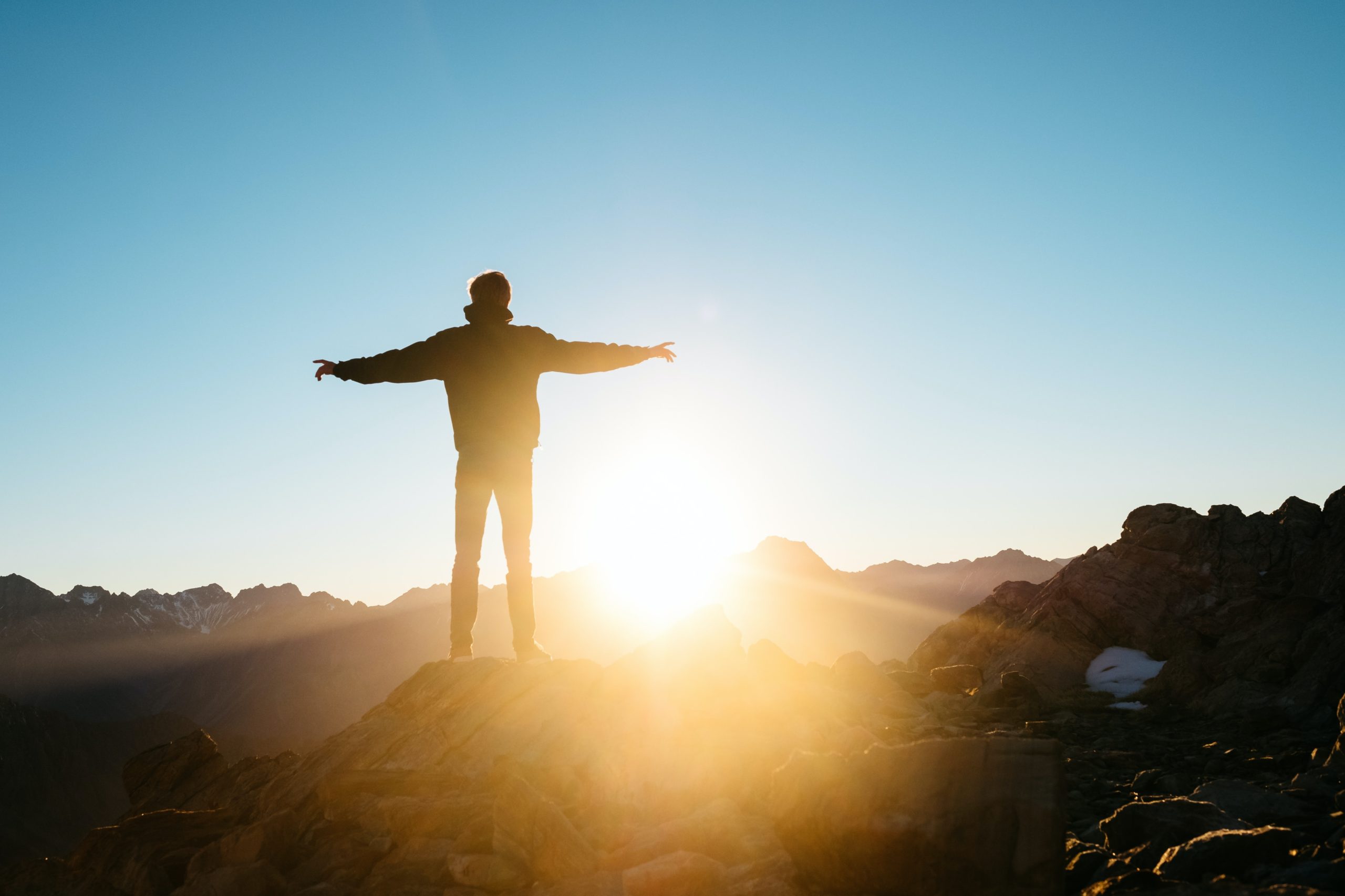 A man spreading his arms on a hill, lit by the rising sun, signifying optimism.