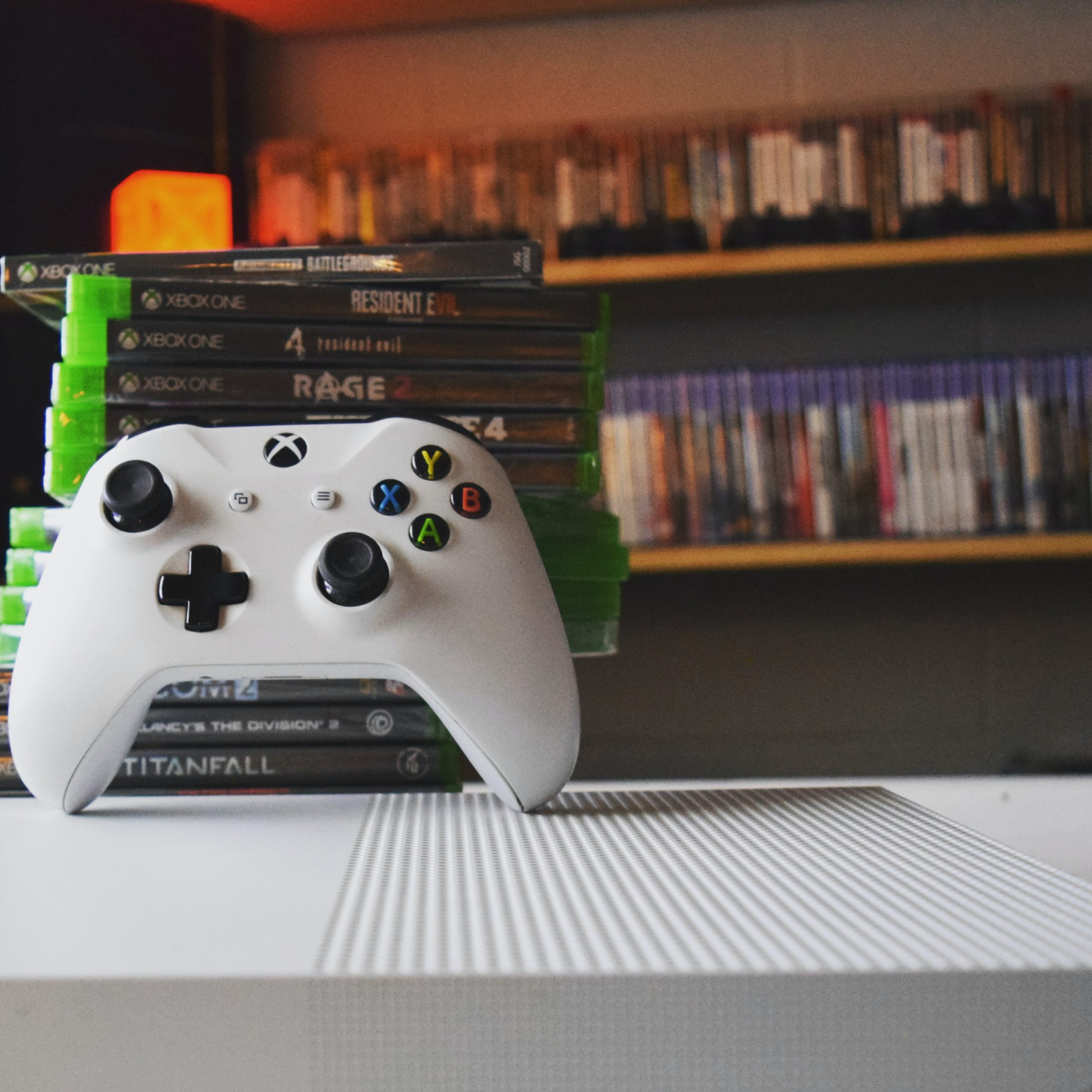 A stack of video games on a table next to a white console controller.