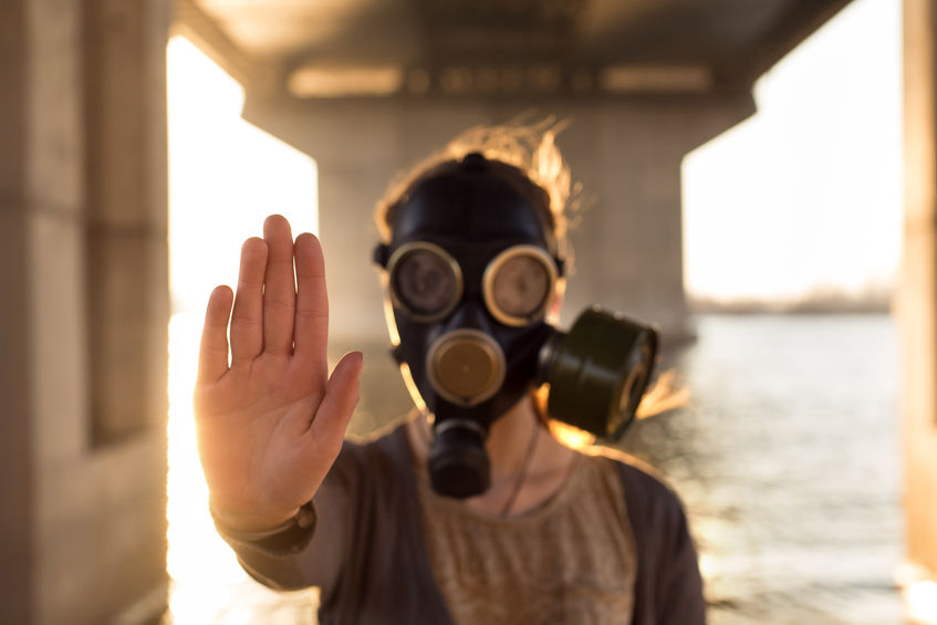 Ecological concept of air contamination. Woman in gas mask near water showing stop gesture