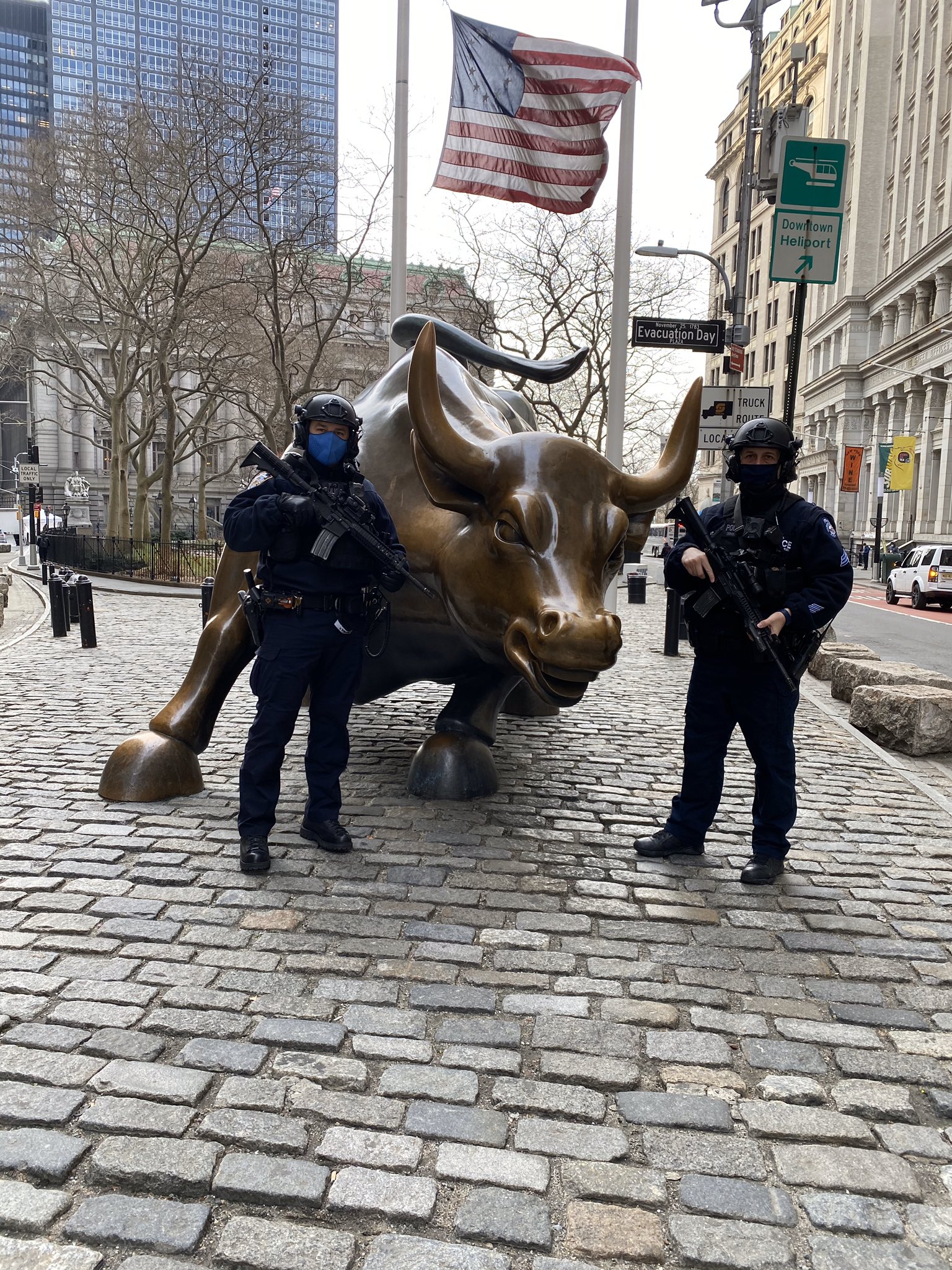 Two armed, mask-wearing police officers with assault rifles guarding Wall Street's Charging Bull