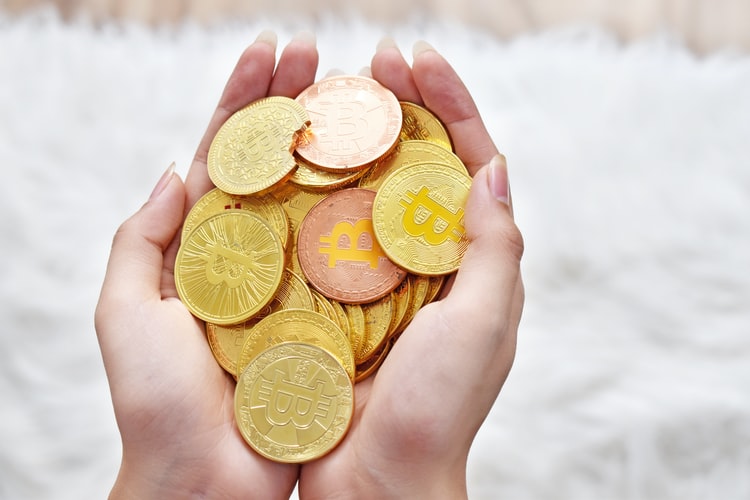 A Caucasian woman holding a handful of golden Bitcoins.