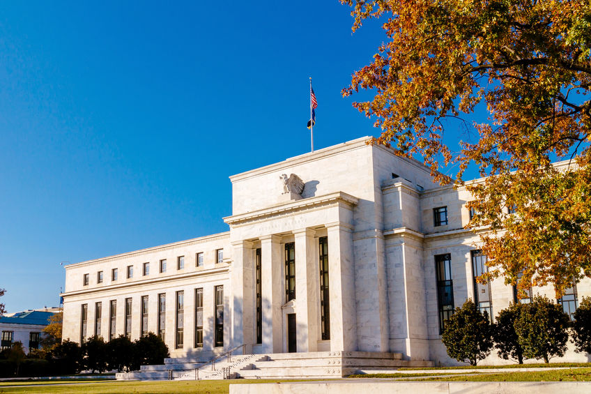 Large, white, marble federal reserve building, in Washington DC. USA, with an eagle statue above the main entrance and an American flag.