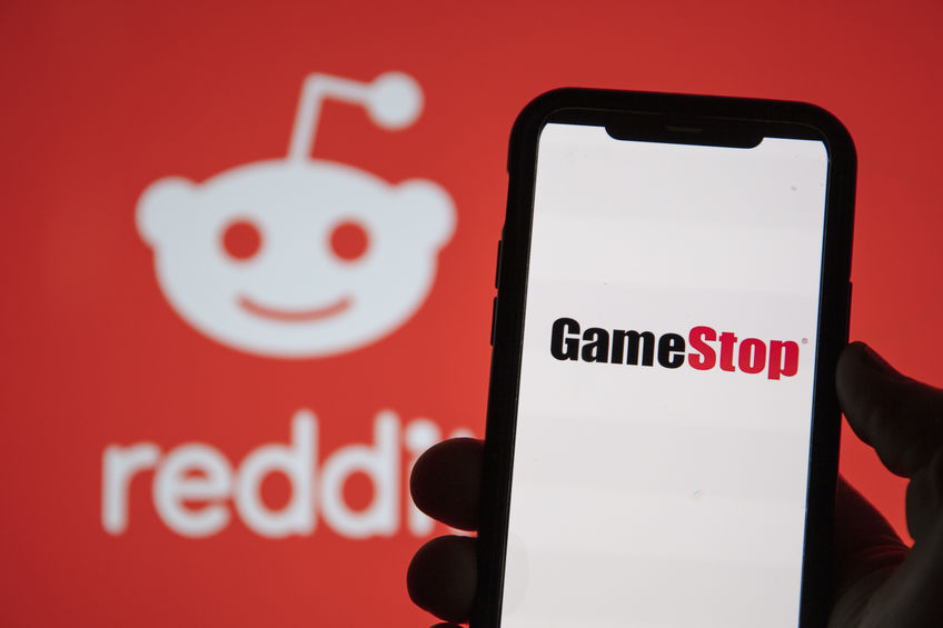Person holding a smartphone with GameStop on Screen and Reddit logo in background