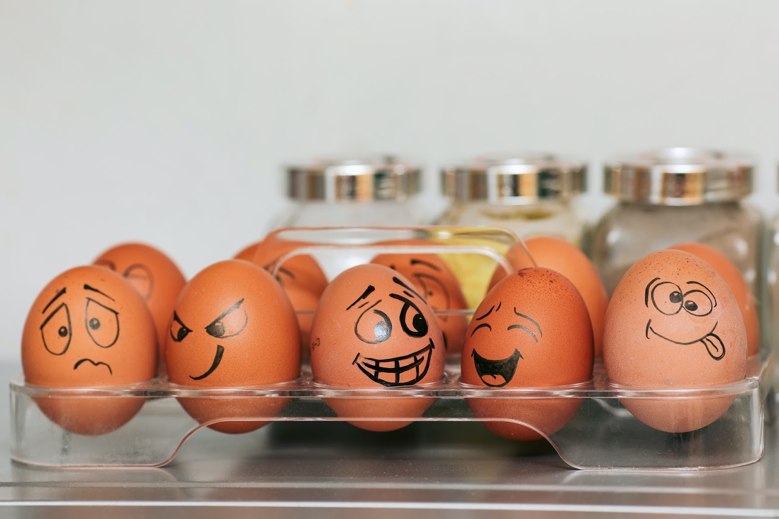 A dozen eggs with funny faces drawn on them.