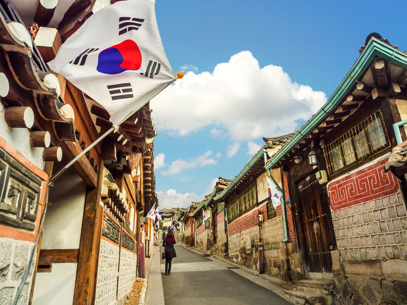 Buildings in South Korea with a blue sky, white clouds, and South Korean flag in background.