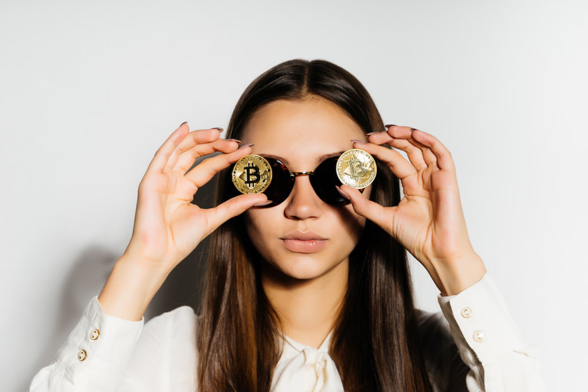 Steep, serious girl with black glasses put a coin to her eyes. Money, electronic money, crypto currency, bitcoins, isolated.
