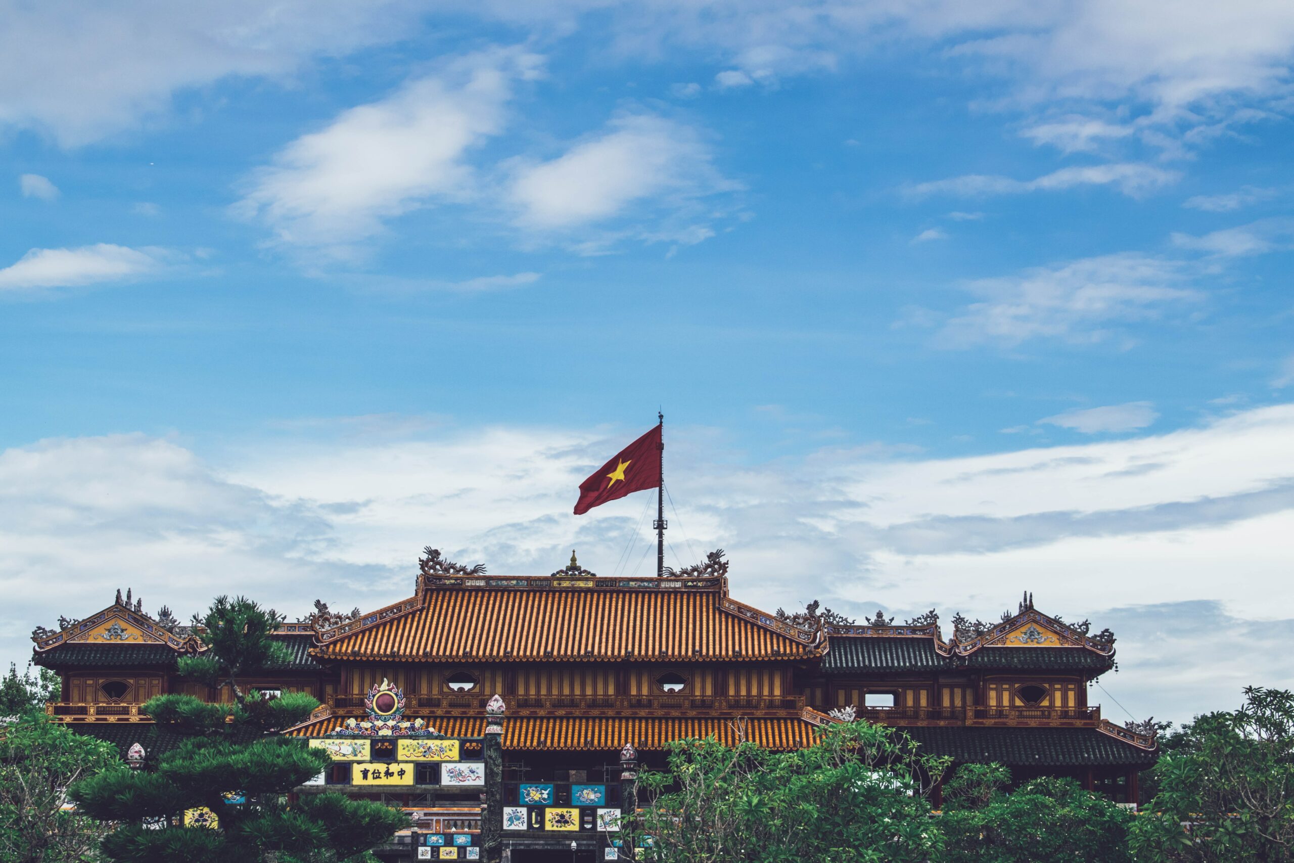 A building in Vietnam with the Vietnamese flag waving in the wind and blue sky in the background.