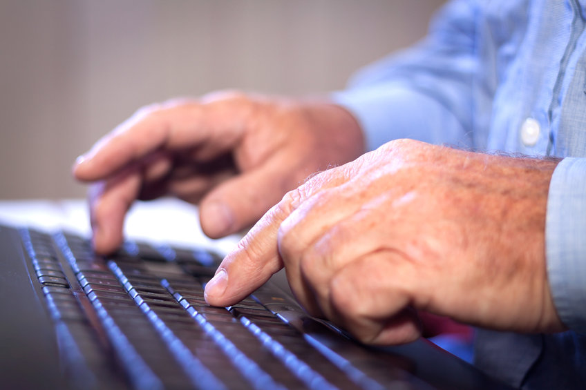 A pair of aged hands type on a laptop keyboard