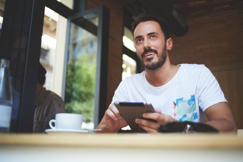 Young man smiling in a cafe and reading about retail traders on reddit using comptershare to own stocks directly.