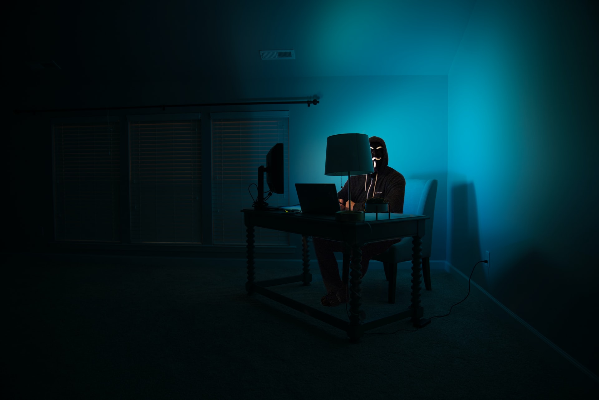 A hacker sitting in a corner working with a computer.
