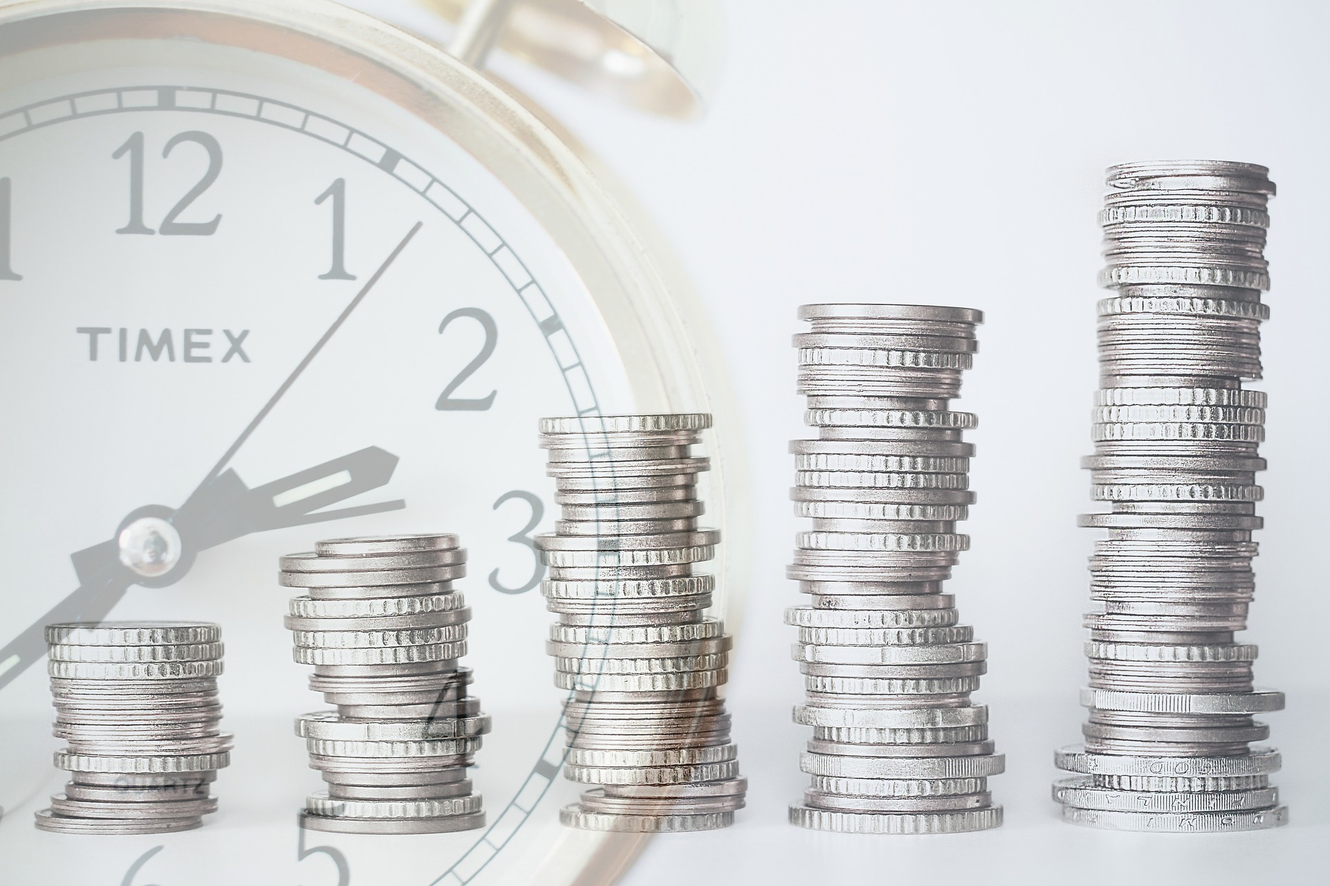 stack of coins with analogue clock ticking in the background