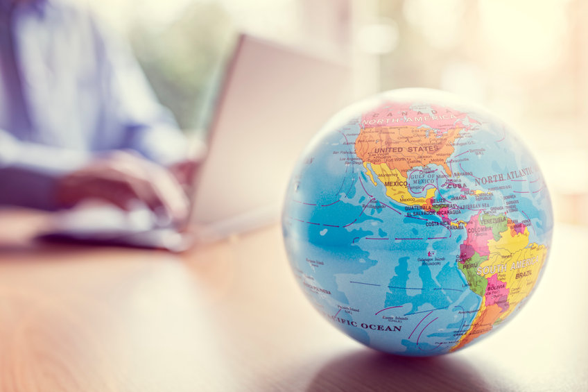 Image of Globe with man on laptop in the background
