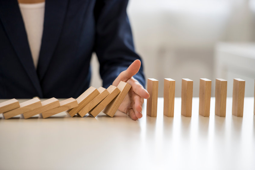 Image of man in suit stopping falling dominos