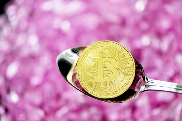 Imahe of a Bitcoin in a spoon with purple gem background