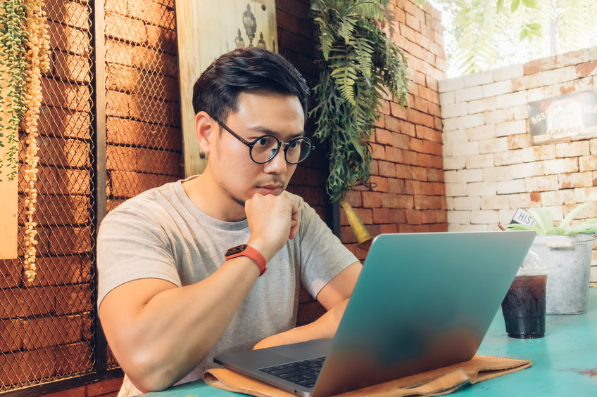 Asian man reading about an Ethereum layer 2 scaling solution called Arbitrum while sitting in a cafe.
